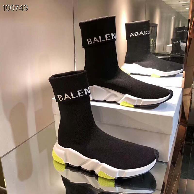 Close-up of black knit fabric and yellow tricolor sole on Speed Trainers