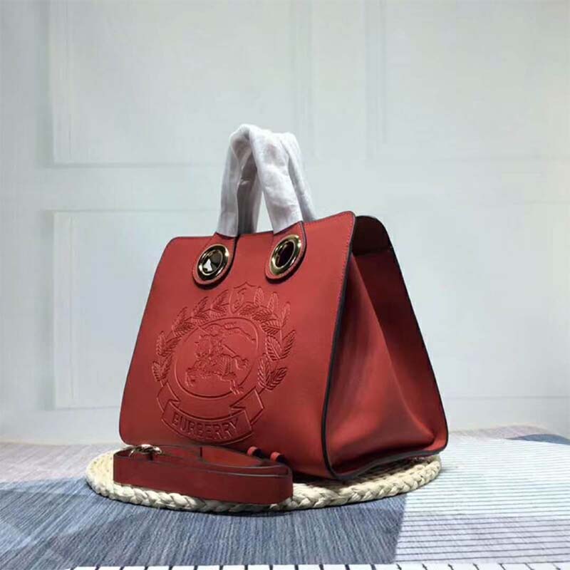 Side angle showing structured silhouette of Burberry Women The Leather Crest Grommet Detail Tote-Red