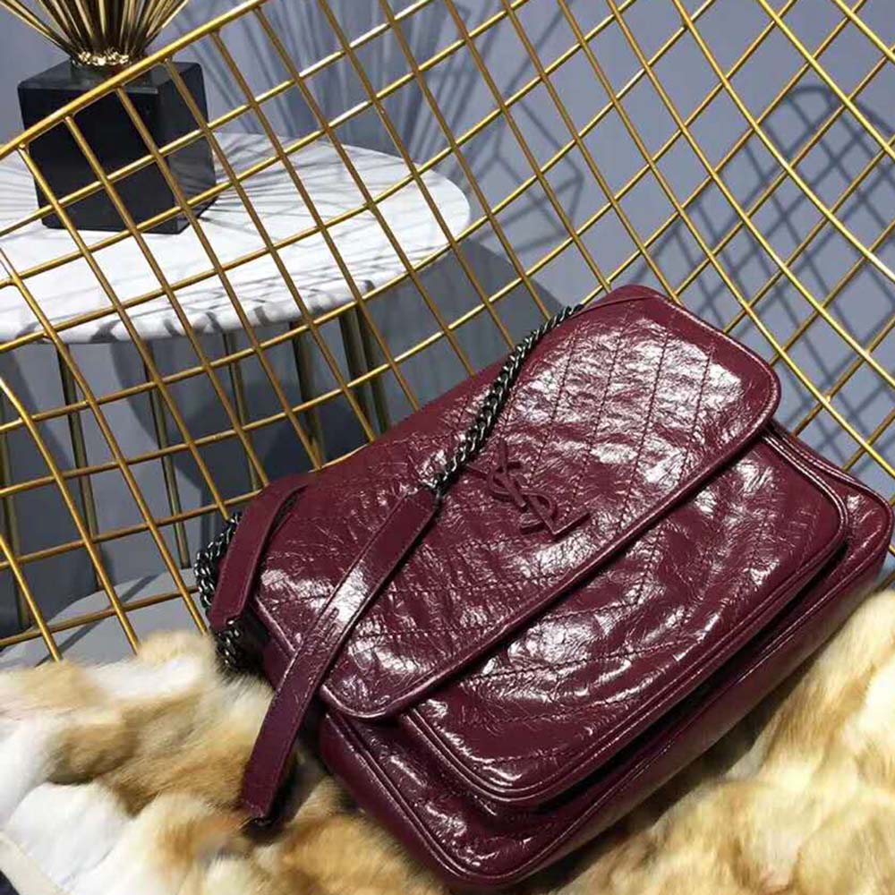Close-up of gold YSL logo and chain closure on maroon leather bag