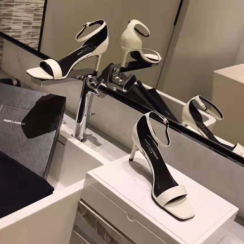 Close-up of gold-tone YSL logo on beige patent leather sandals
