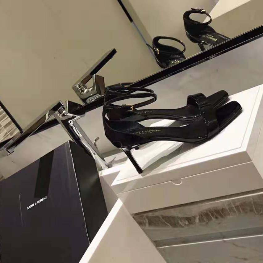 Close-up on gold YSL logo detail on black patent leather sandal strap