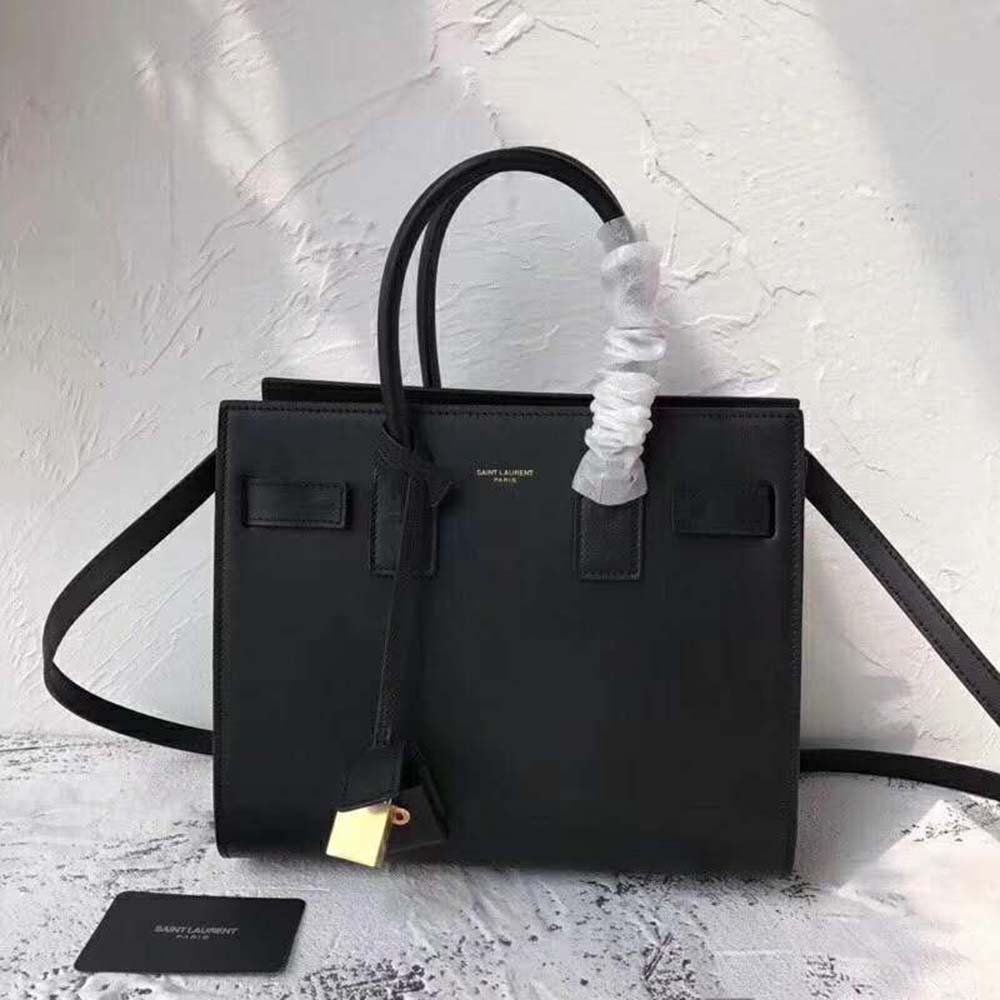 Close-up detail of gold YSL logo on smooth black leather bag