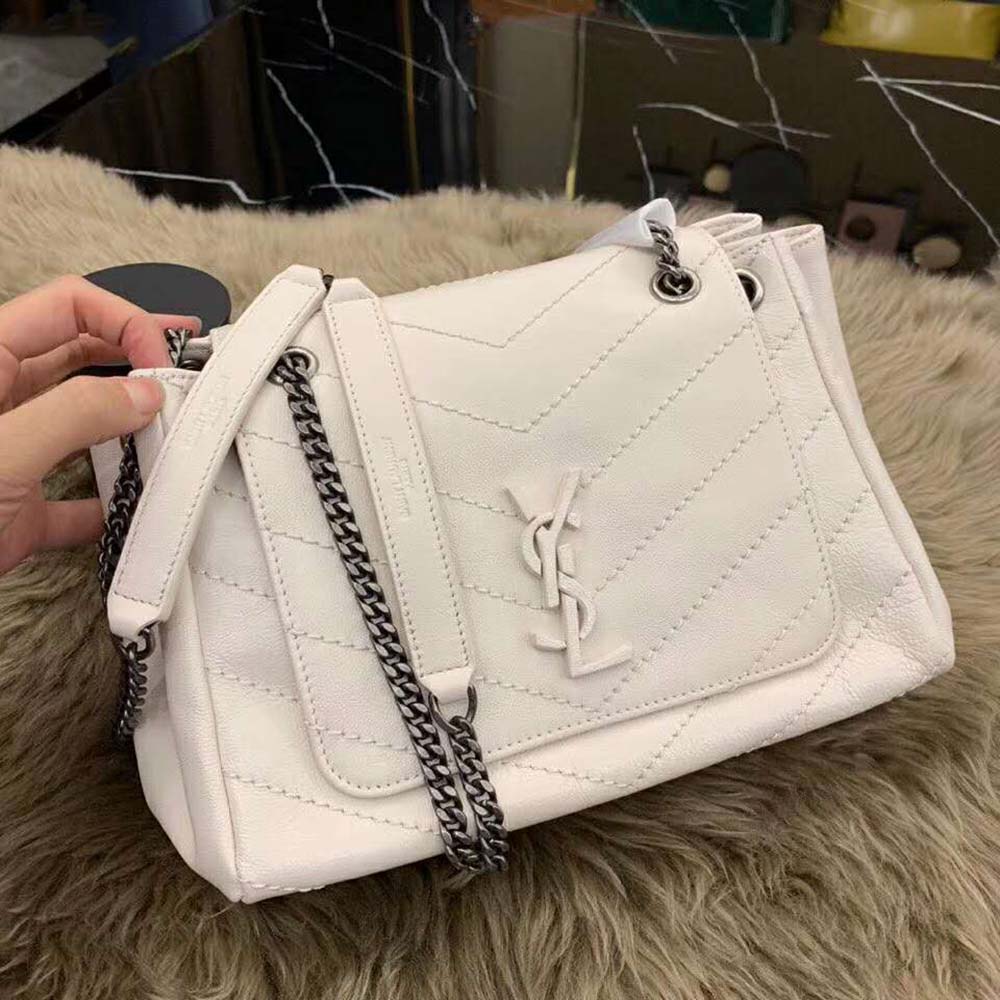 Close-up of gold YSL logo hardware on white vintage leather bag