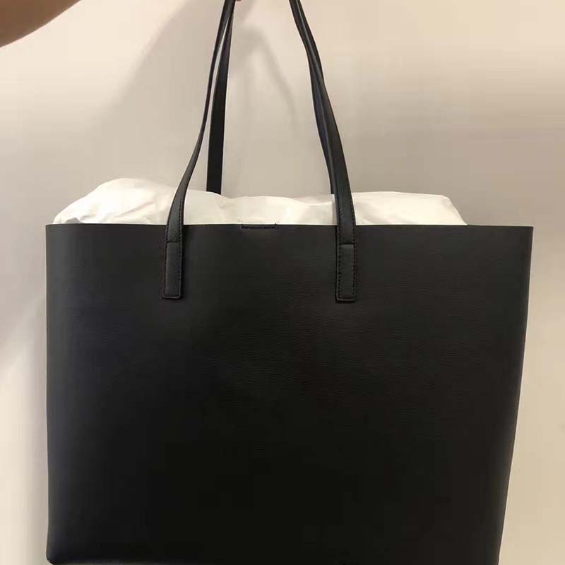 Close-up of gold-tone YSL logo on black leather tote
