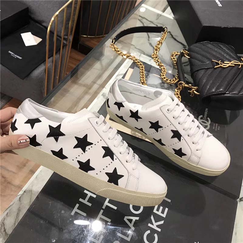 Close-up of gold YSL logo hardware on white leather sneaker