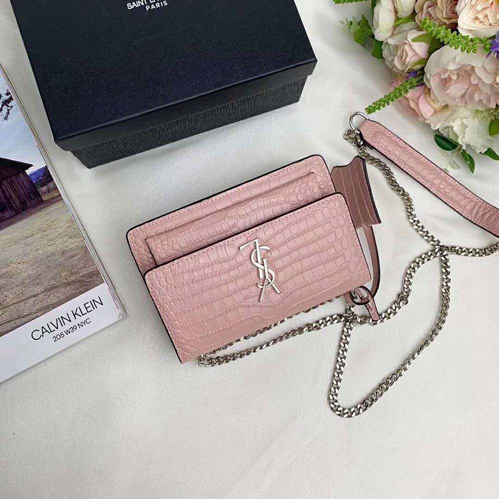 Close-up of gold YSL logo hardware on shiny-pink crocodile-embossed bag