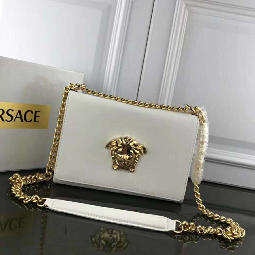 Close-up of gold Medusa head hardware on white clutch bag