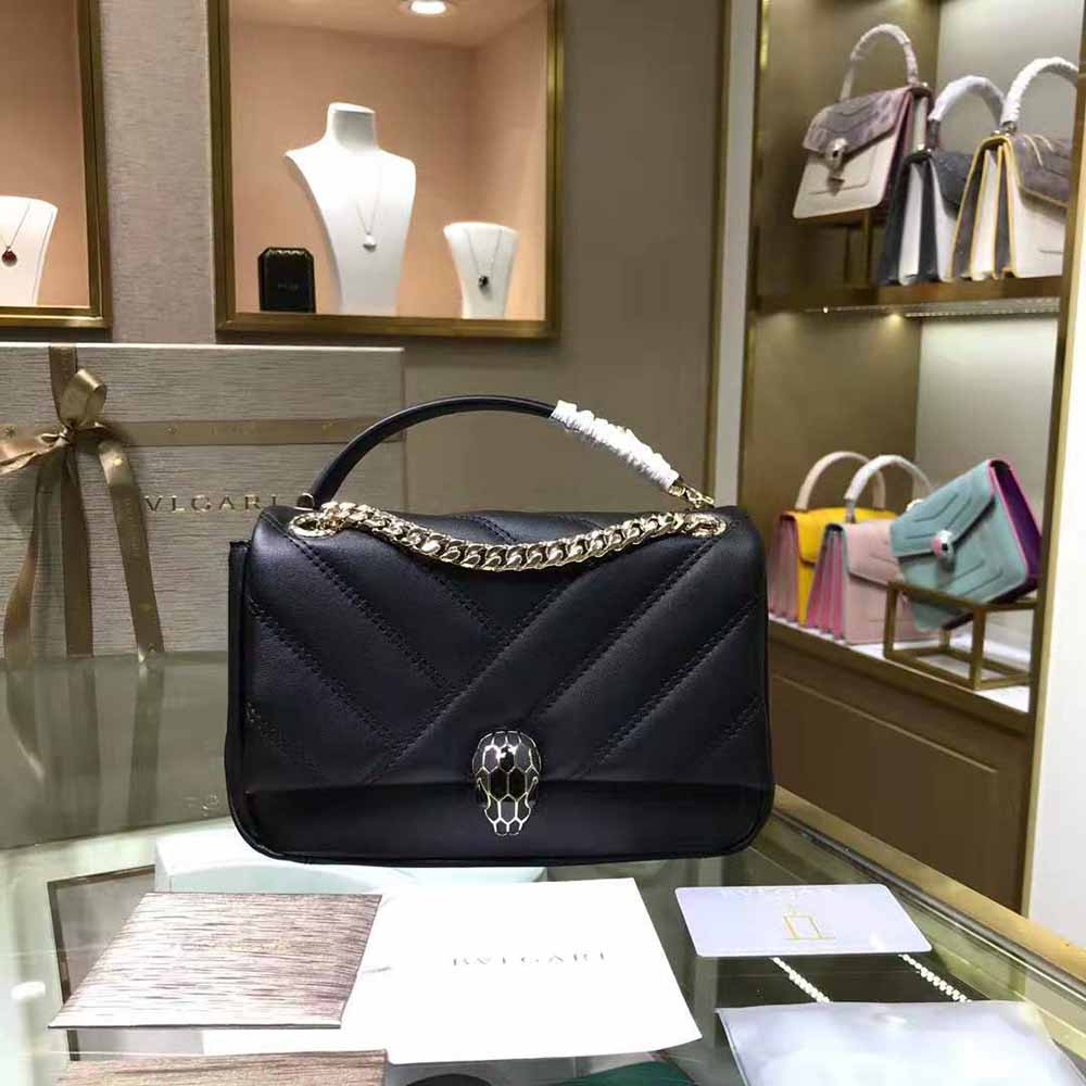 Close-up detail of gold-tone Serpenti cabochon clasp on black leather shoulder bag