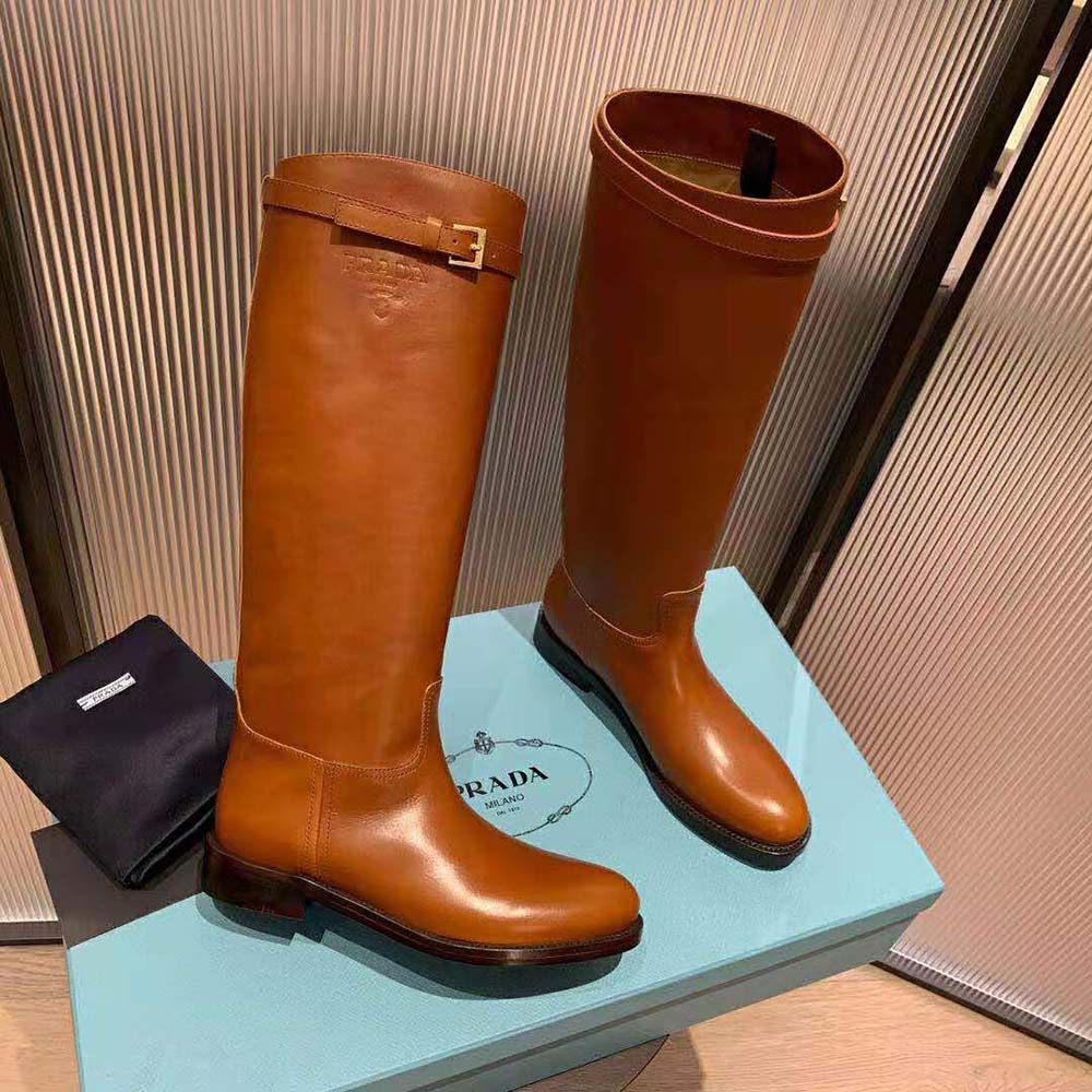 Close-up of polished gold-tone Prada logo on brown leather boots