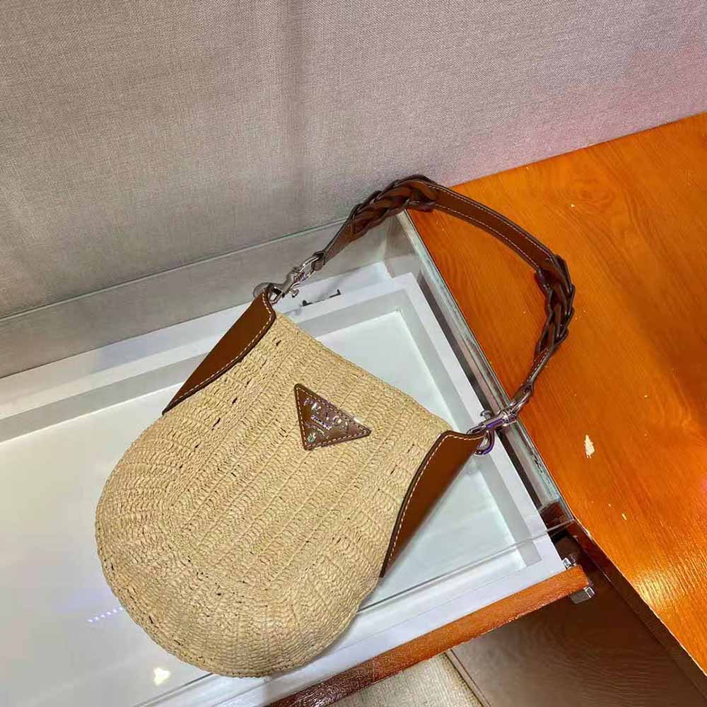 Close-up detail of gold-tone Prada logo on raffia and leather bag