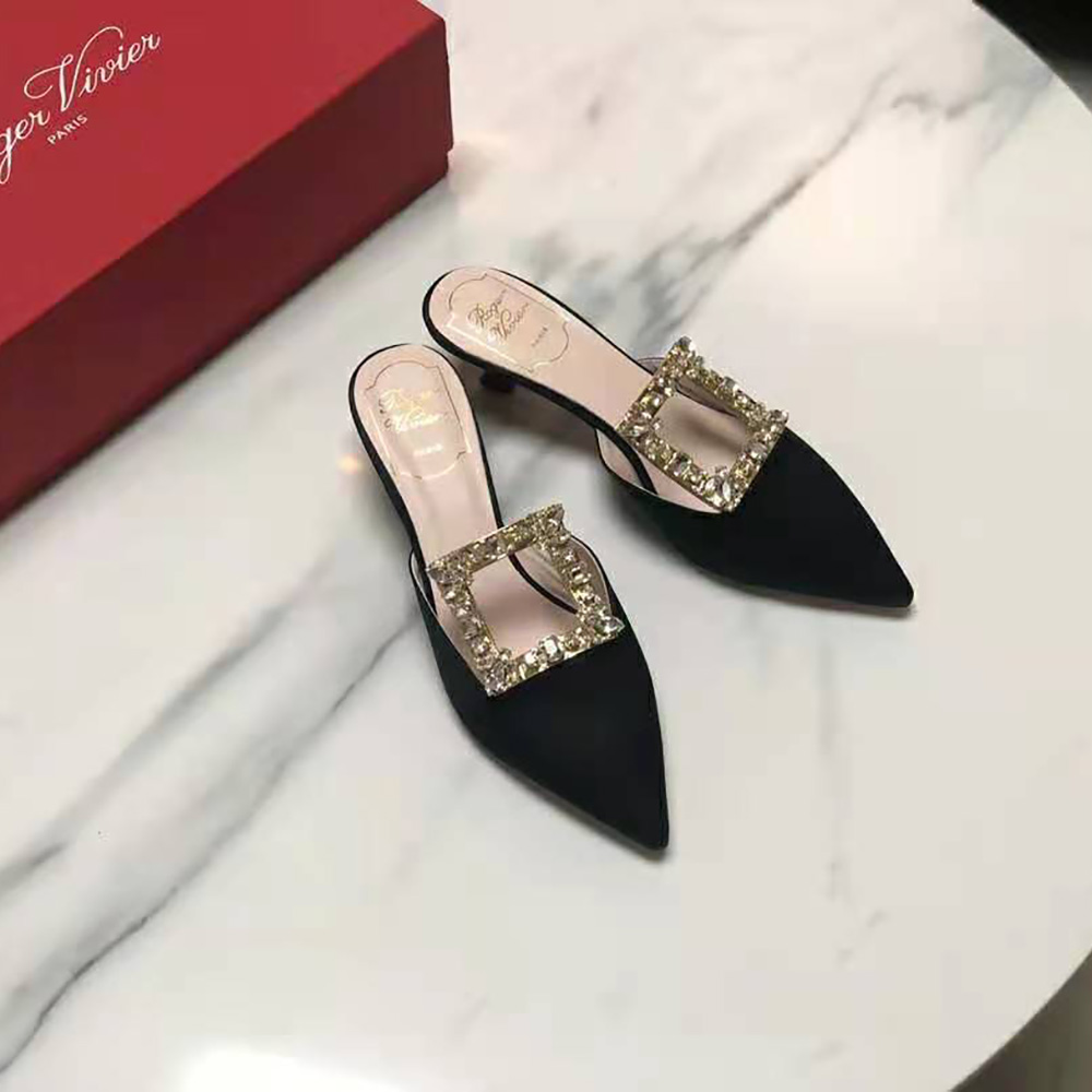 Close-up of signature silver broche buckle on black satin mules