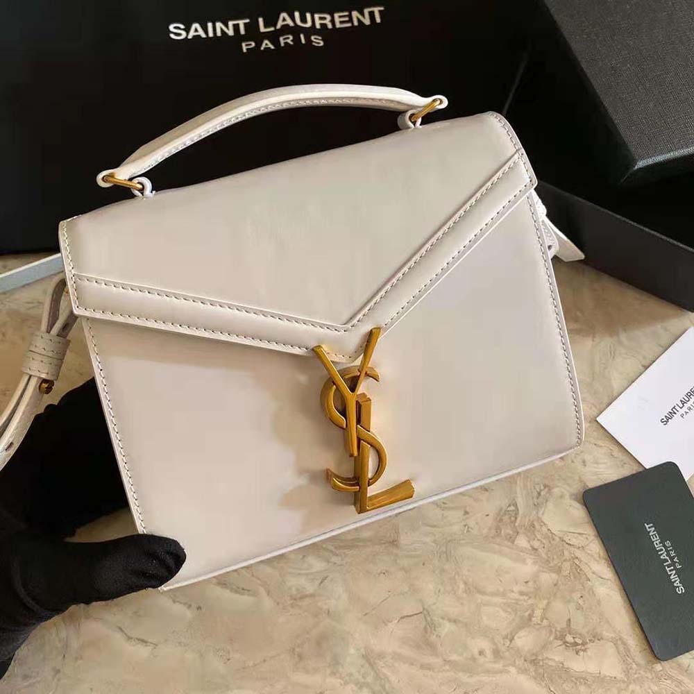 Close-up of gold YSL emblem on white Cassandra Mini Top Handle bag