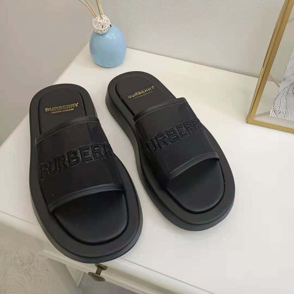 Close-up of embroidered Burberry logo on black mesh and leather slides
