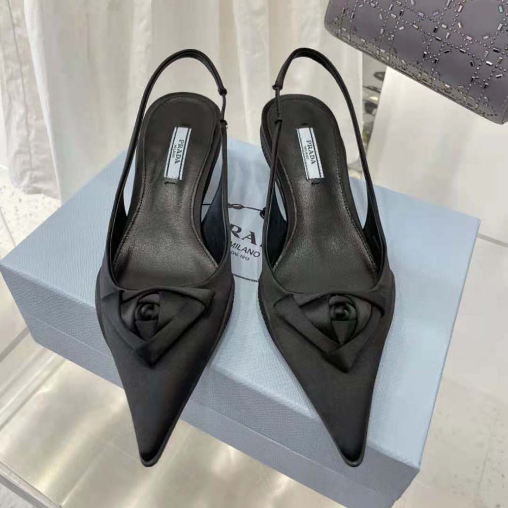 Close-up detail of Prada logo hardware on black nylon slingback pumps