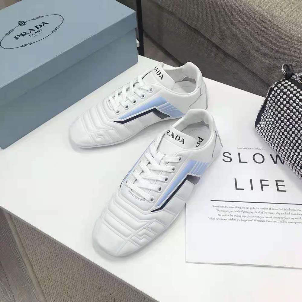 Close-up on embossed Prada logo hardware on white leather sneakers
