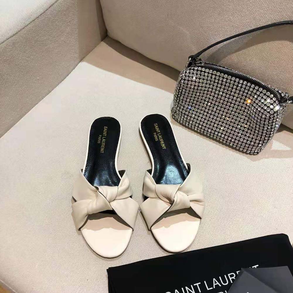 Close-up on gold YSL logo hardware on white leather mules
