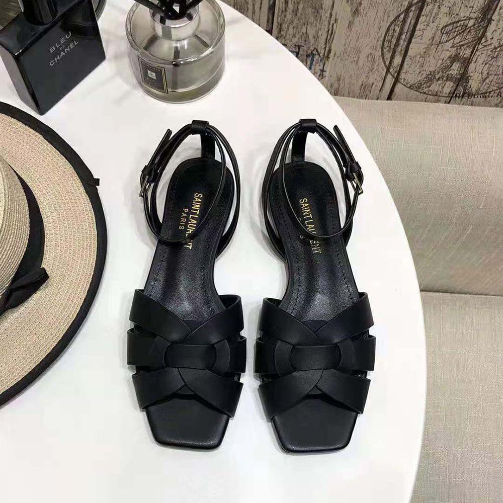 Close-up of gold YSL logo hardware on black sandals
