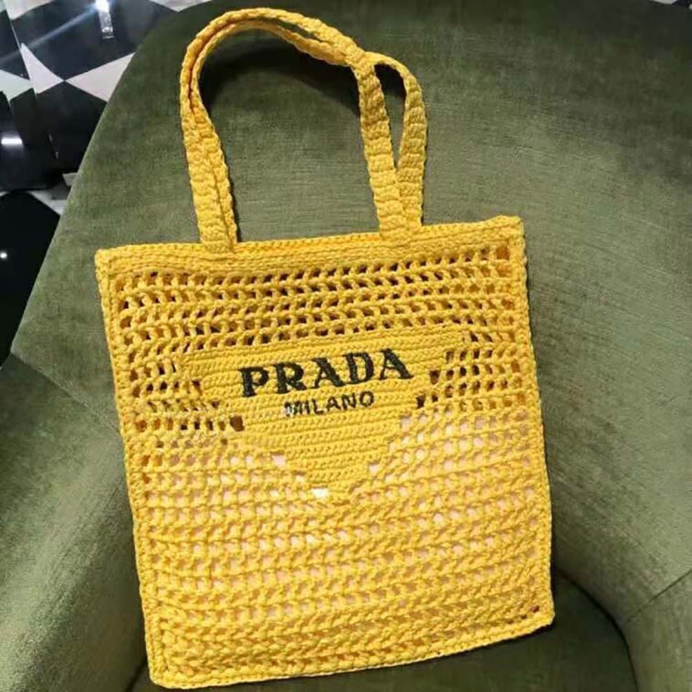Close-up of gold Prada logo hardware on yellow raffia tote bag
