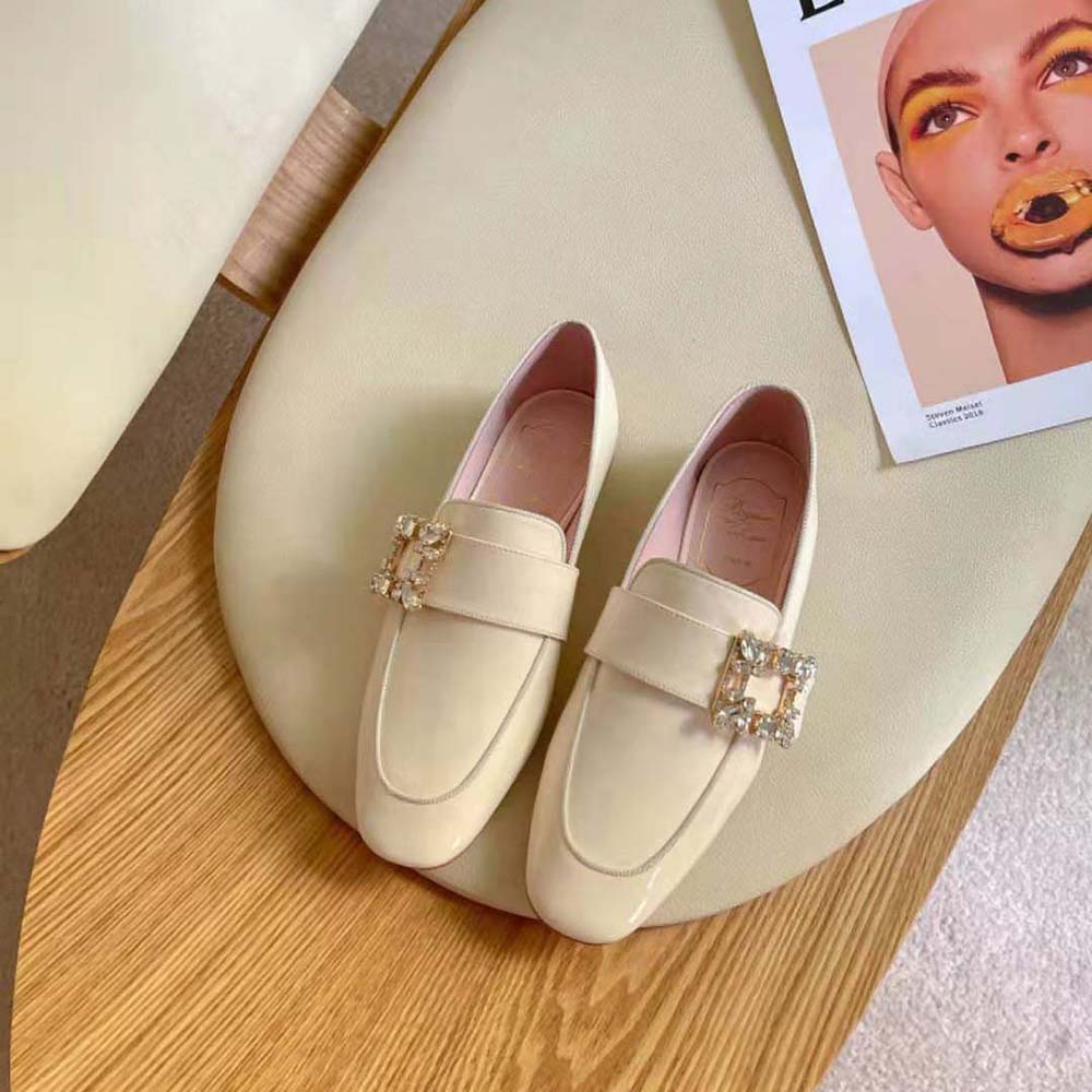 Close-up of signature Mini Broche buckle on white patent leather loafers