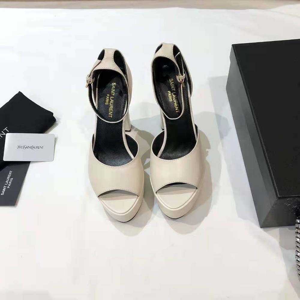 Close-up of signature YSL logo hardware on white Jodie Platform Sandals
