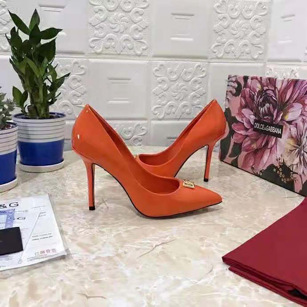 Close-up of gold DG logo hardware on orange Dolce Gabbana patent leather pumps
