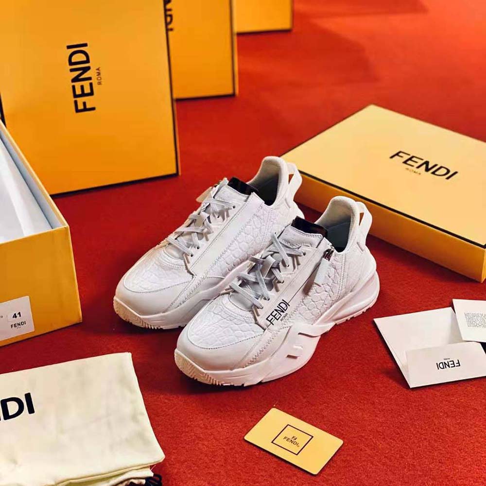 Side view highlighting gold-tone Fendi logo on white caiman sneakers