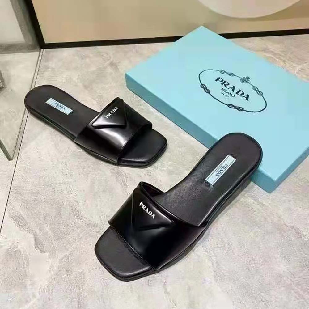Close-up of the triangular Prada logo on black leather slides