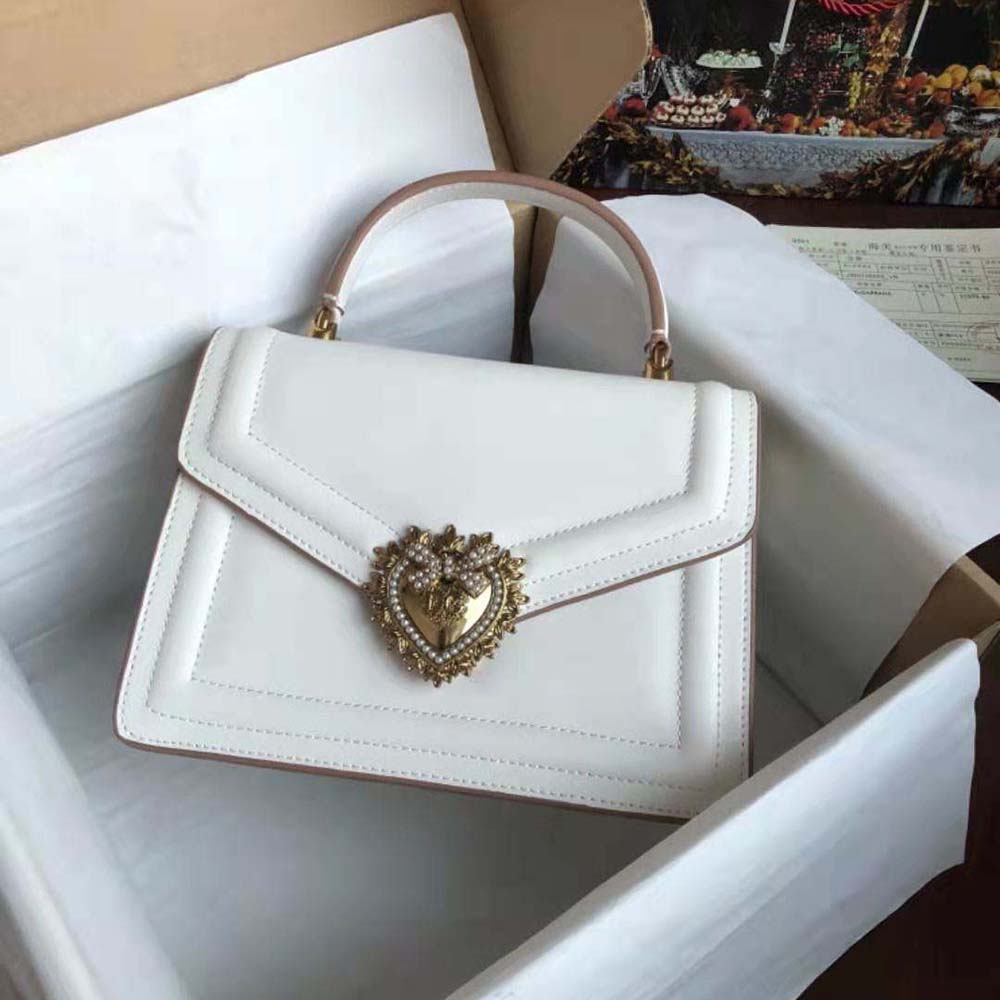 Close-up of gold-tone Devotion heart clasp on white handbag