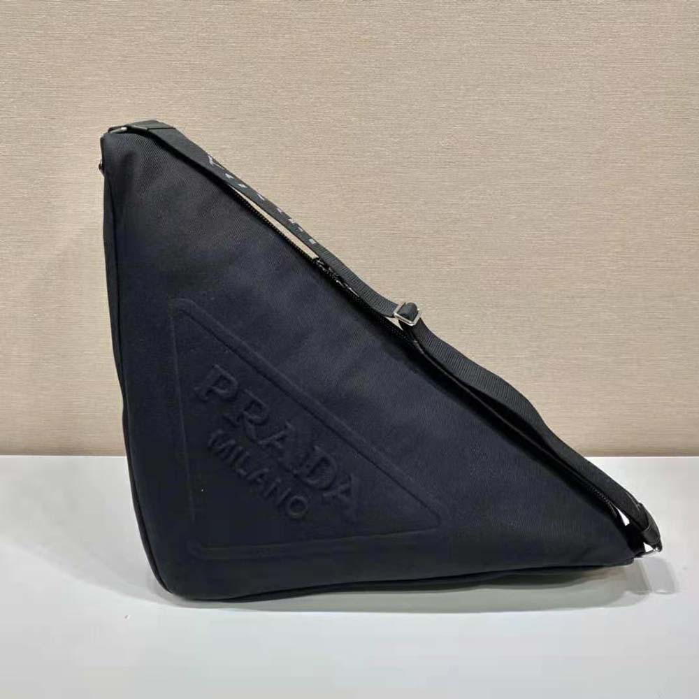 Close-up of silver Prada triangle logo on black canvas bag