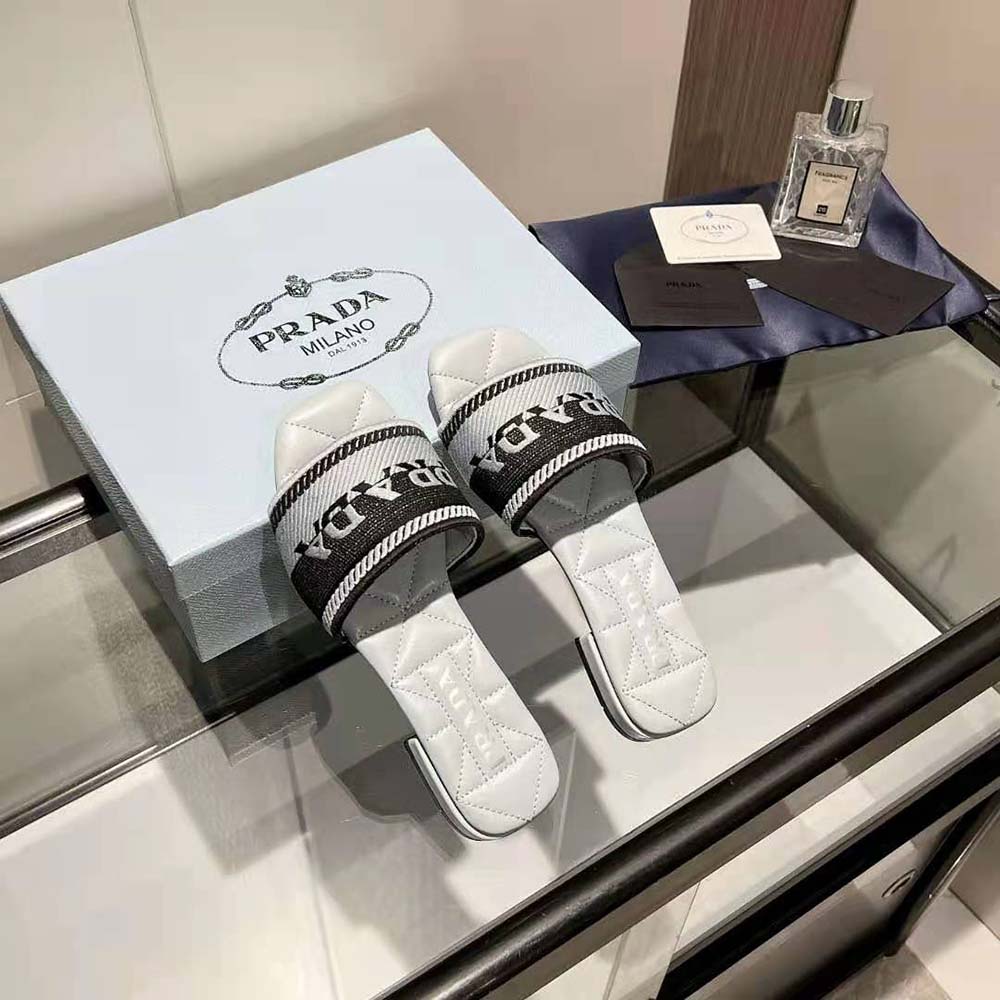 Close-up of embroidered Prada lettering on white fabric slides