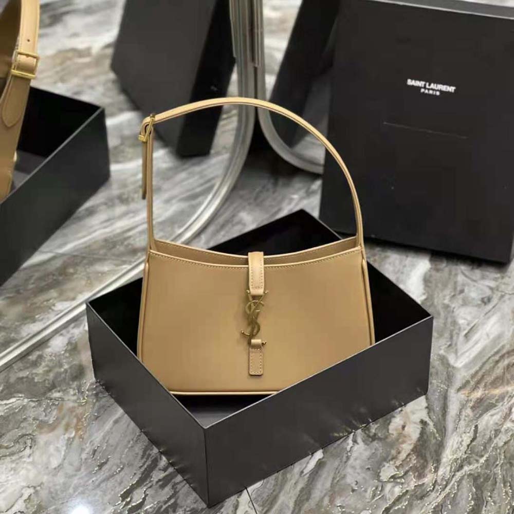 Close-up of gold YSL logo hardware on sandy leather hobo bag