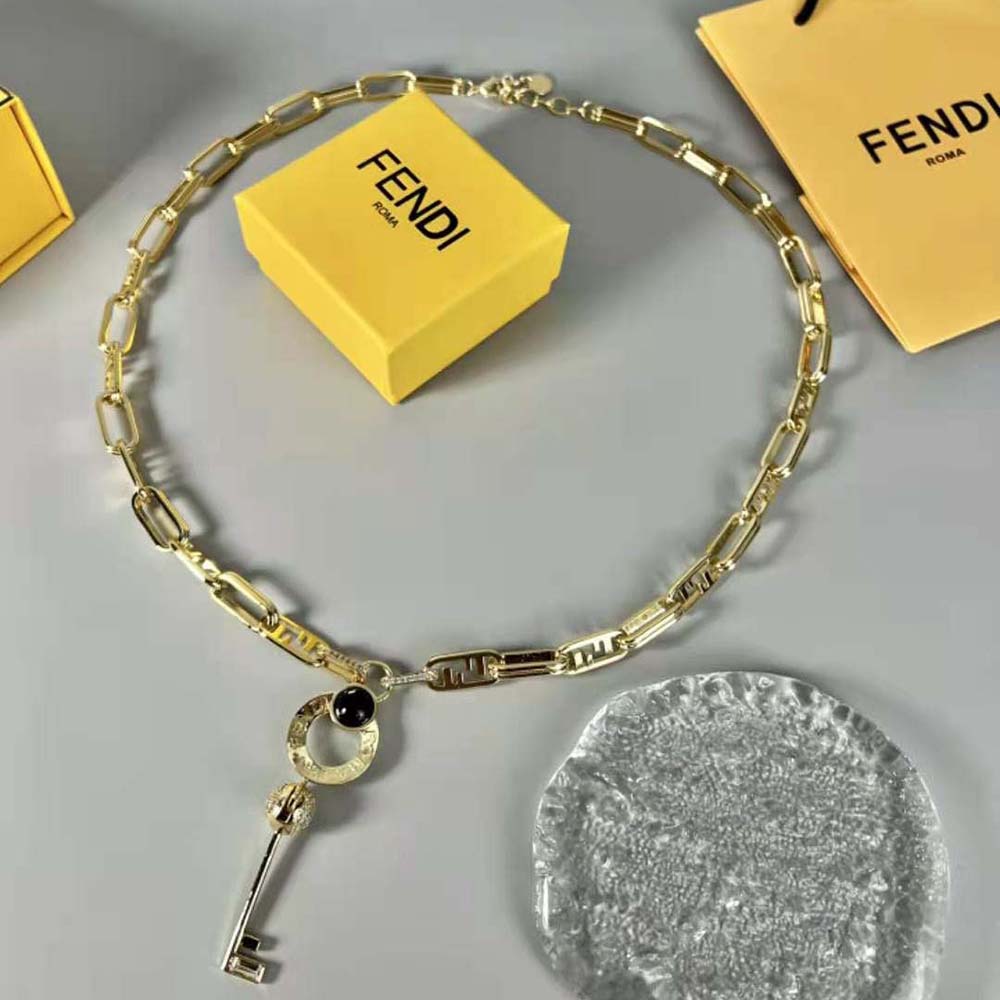 Close-up detail of signature Master Key charm on gold-colored necklace