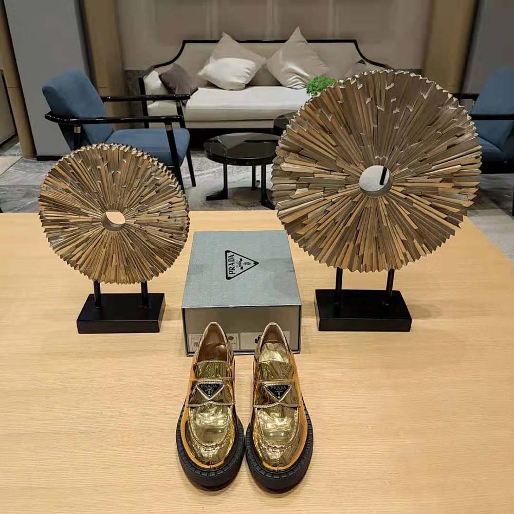 Close-up on golden Prada logo hardware on metallic leather loafers