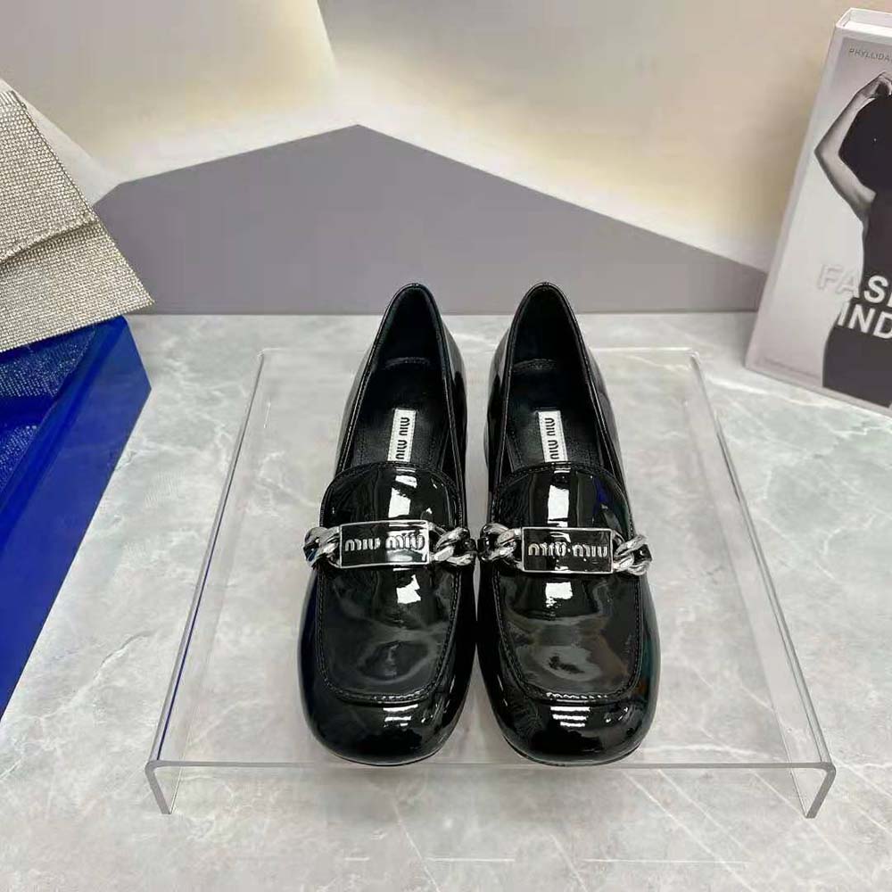 Close-up detail of Miu Miu logo on black patent leather loafer