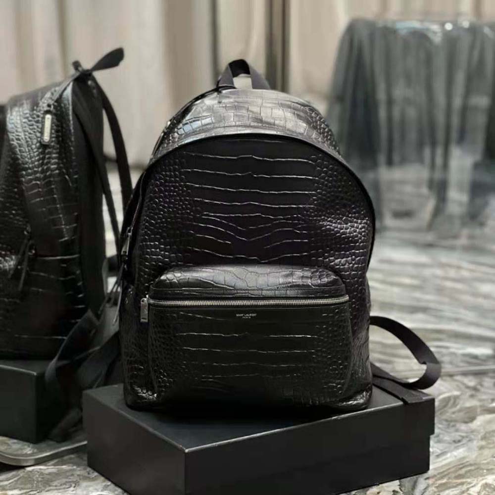 Close-up of gold YSL logo hardware on black crocodile-embossed backpack