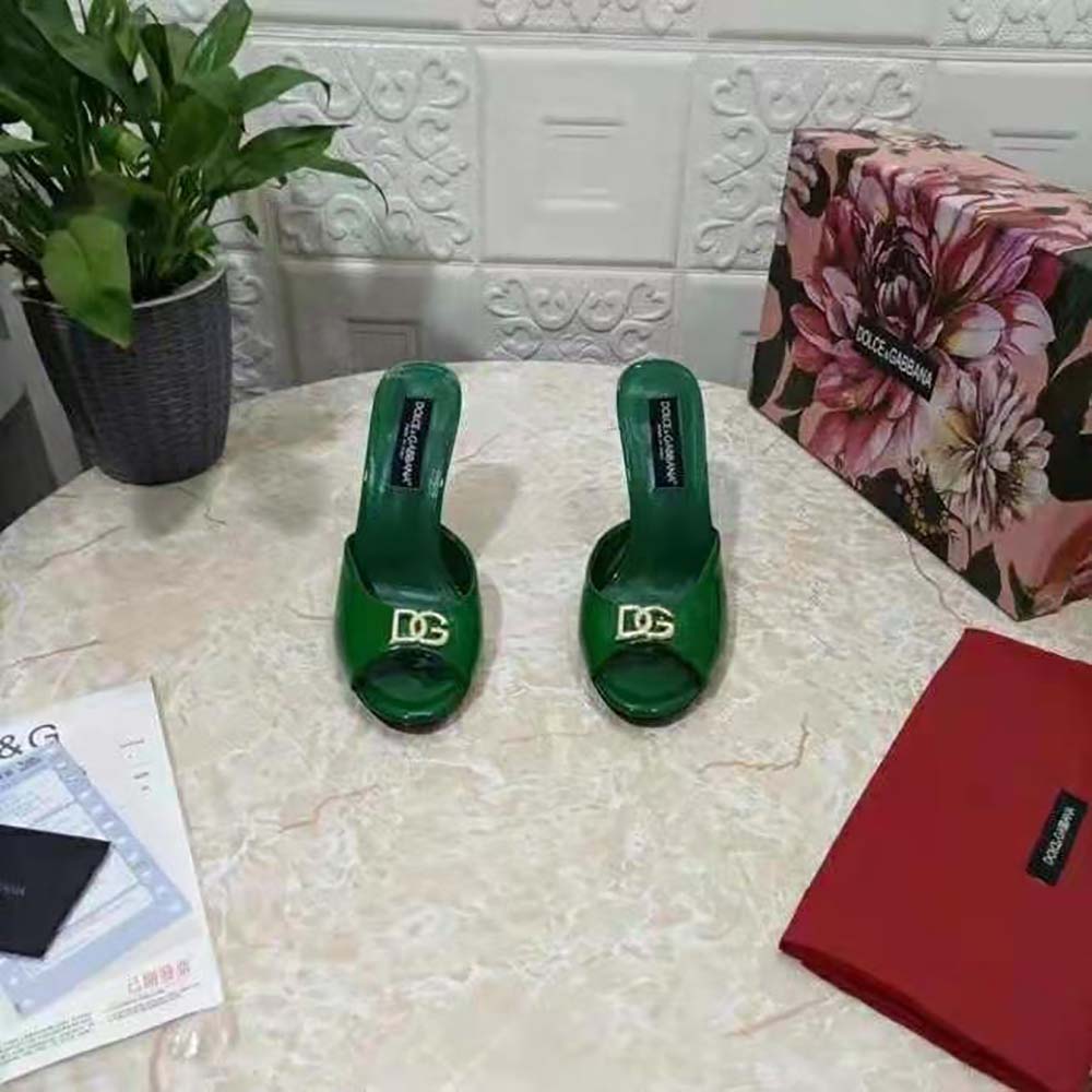 Close-up of gold DG logo hardware on green patent leather mules
