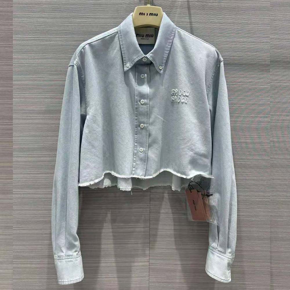 Close-up of embroidered Miu Miu logo on blue denim shirt