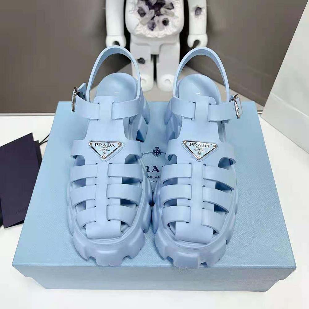 Close-up detail of blue Prada sandals showing glossy enameled triangle logo hardware