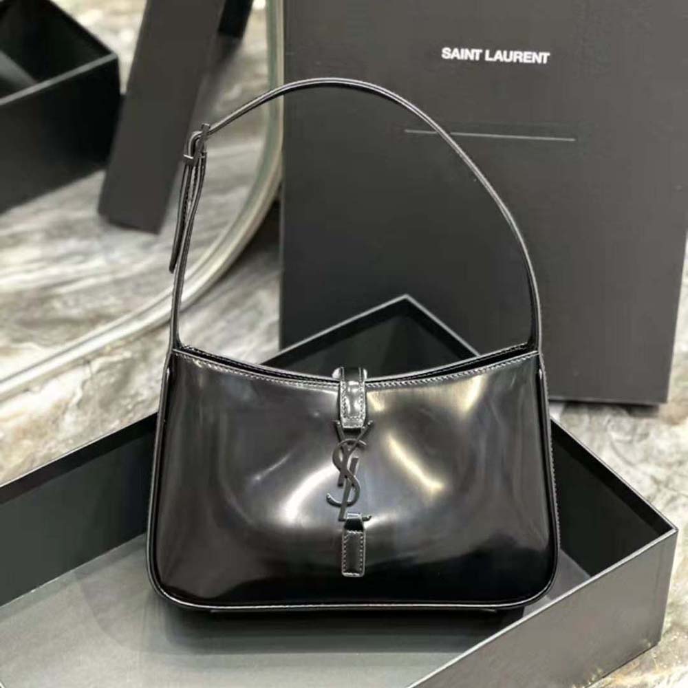 Close-up of gold-tone YSL logo on shiny black leather bag