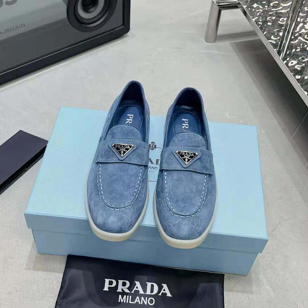 Close-up of enameled Prada triangle logo detail on blue suede loafer