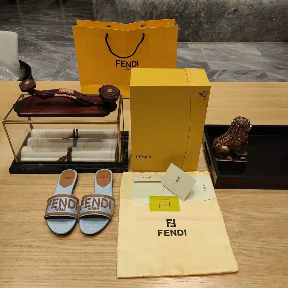 Top-down angle highlighting gold-tone Fendi logo on denim slides