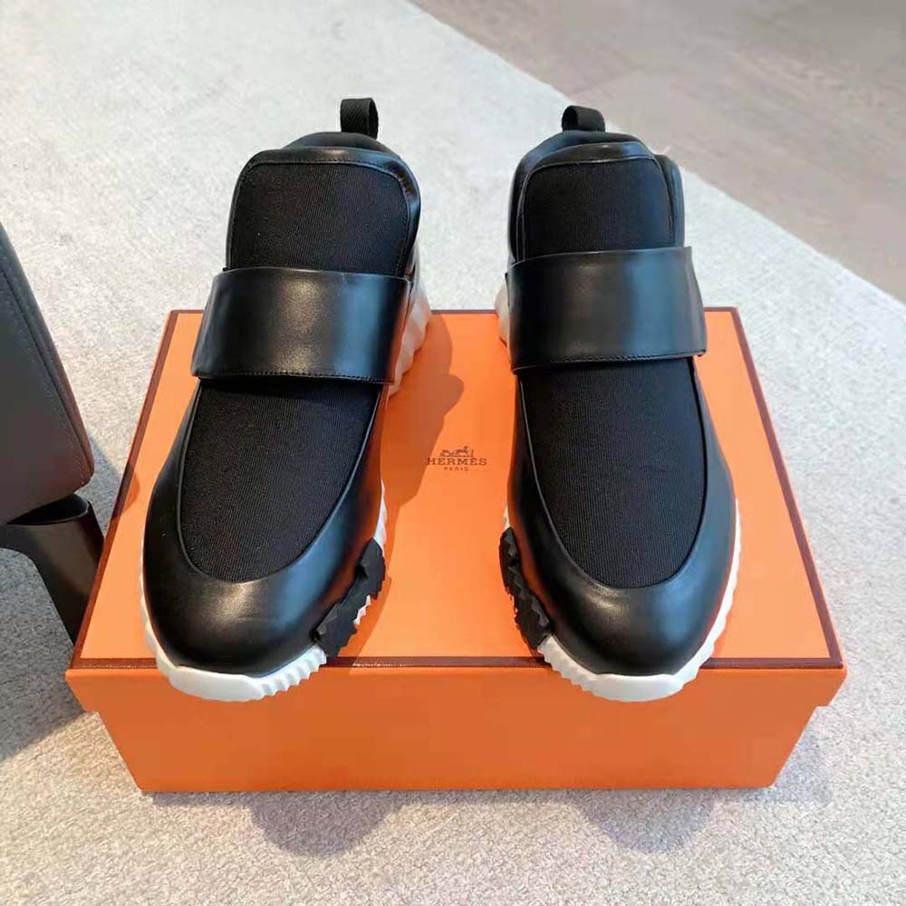 Close-up detail of Hermes H metal hardware on black sneaker