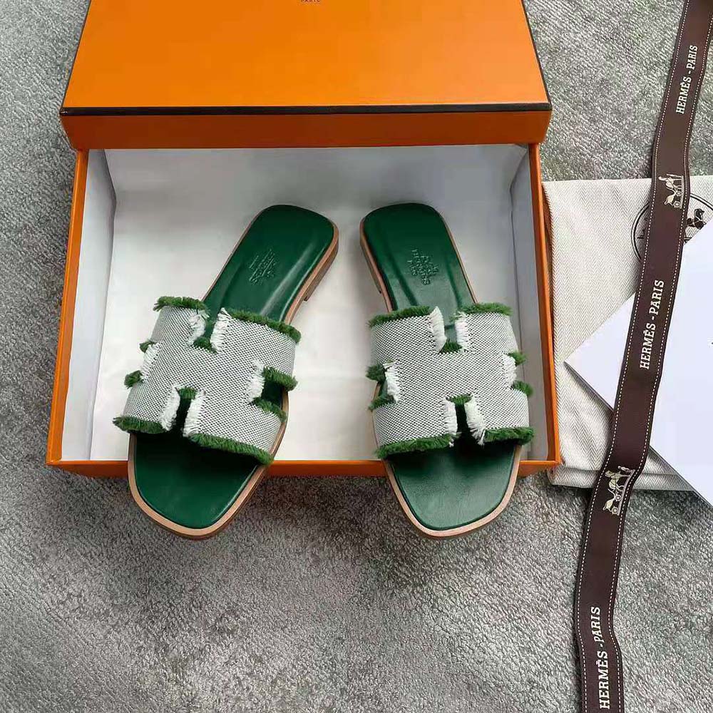 Close-up of Hermes signature H cutout on green fringed canvas sandal