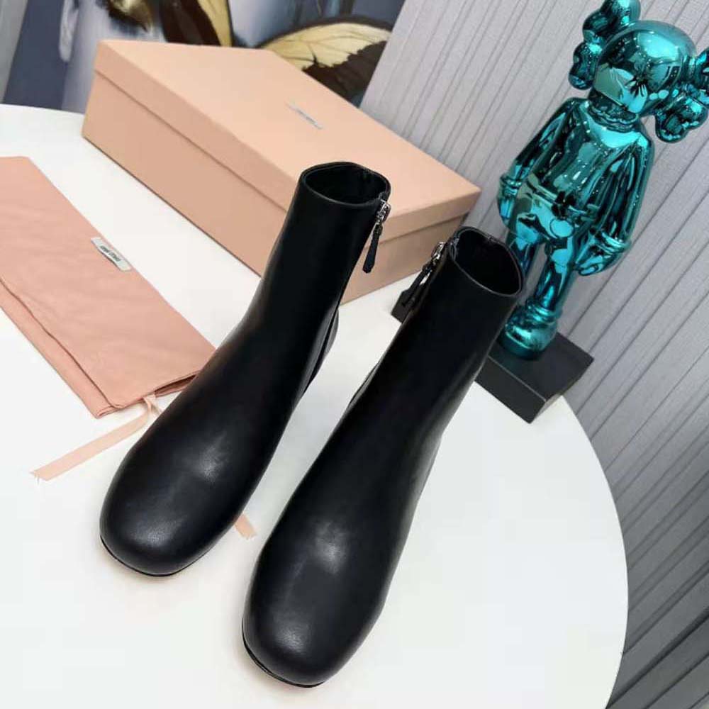 Close-up of metal lettering logo on Miu Miu black leather booties