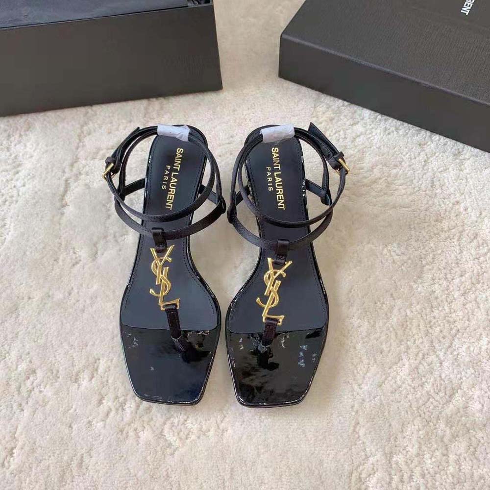 Close-up of gold YSL logo hardware on Cassandra Sandals in black silk satin