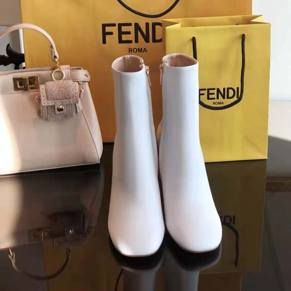 Close-up detail of gold Fendi emblem on white leather boot