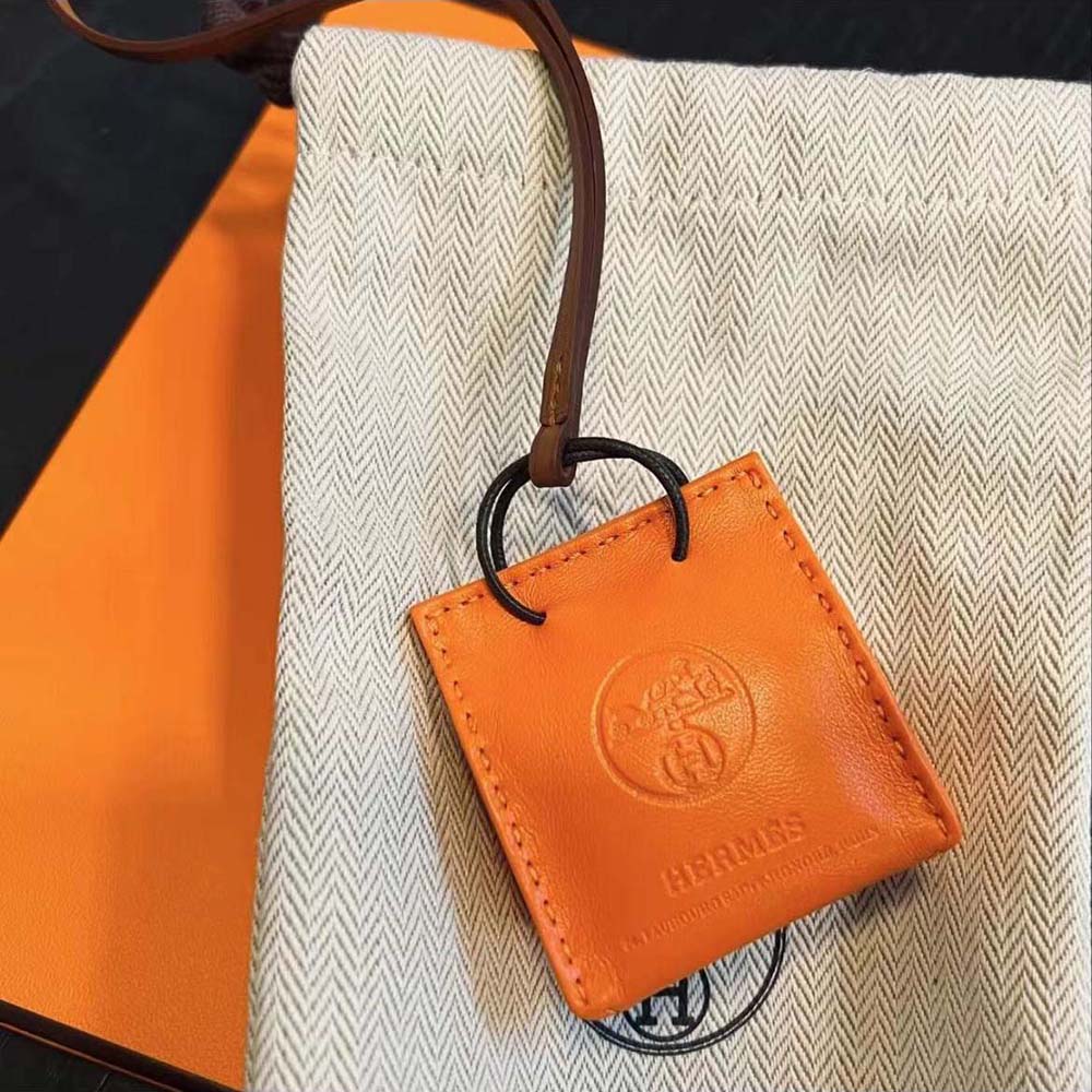 Hermes Orange Bag Charm attached to a luxury handbag handle