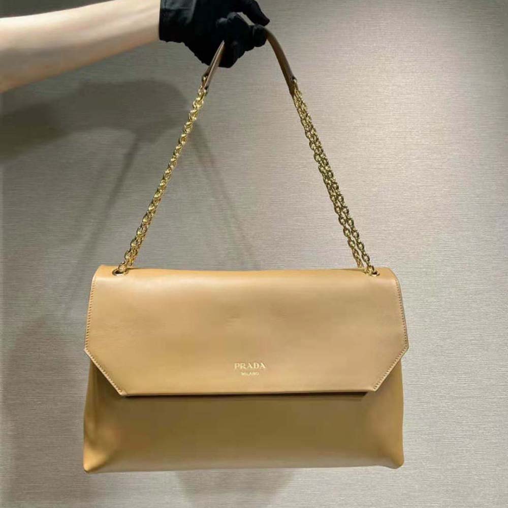 Close-up on gold-tone Prada logo plaque on brown leather shoulder bag