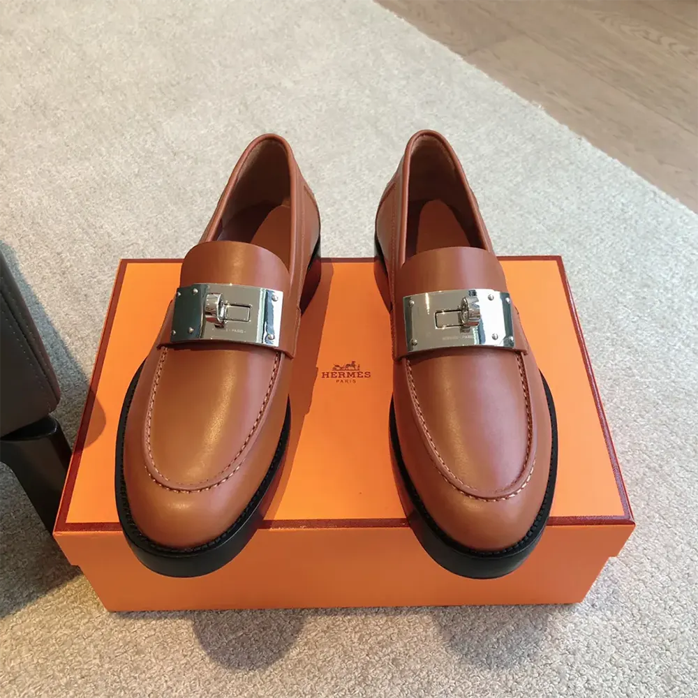 Close-up of signature Hermes silver hardware detail on brown loafer