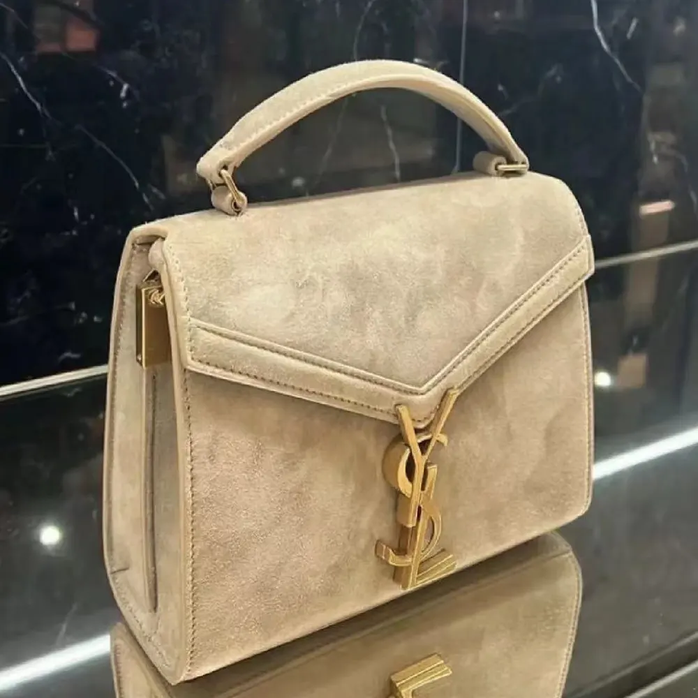 Close-up of gold YSL logo hardware on beige suede Cassandra Mini bag